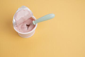 Yogurt in a plastic cup with a spoon on a colored background, top view. Space for text