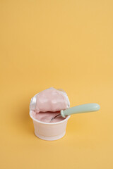 Yogurt in a plastic cup with a spoon on a colored background, top view. Space for text.