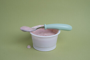 Yogurt in a plastic cup with a spoon on a colored background, top view. Space for text.
