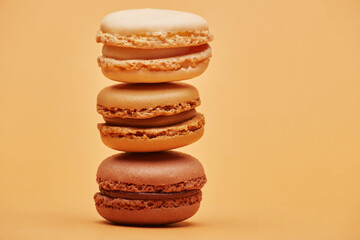 Stack of three biscuits macaron cookies chocolate vanilla and light beige color isolated on the bright solid fond plain bright sandy beige background