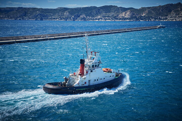 Marine tugboat heading out from harbor into rough sea, powerful waves and clear skies
