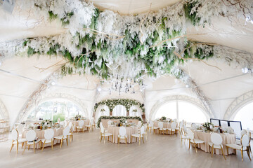 Elegant wedding reception hall featuring round tables, white and gold chairs, and floral...