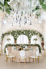 Elegant wedding reception hall featuring round tables, white and gold chairs, and floral arrangements