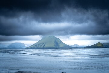 View of a lone green mountain peak emerging from the cloud cover above the icy landscape, against the skyline, Kirkjubaejarklaustur, SkaftÃ¡rhreppur, Iceland.