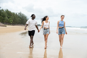 Group of diverse young friends black man and women in casual relaxing and walking on tropical beach...