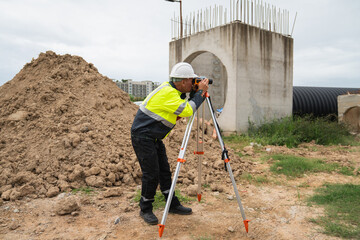 The survey team is using a theodolite and road construction plans. Civil engineers are measuring with surveying tools during the construction