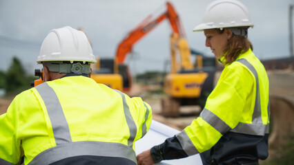 The survey team is using a theodolite and road construction plans. Civil engineers are measuring with surveying tools during the construction
