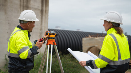 The survey team is using a theodolite and road construction plans. Civil engineers are measuring with surveying tools during the construction
