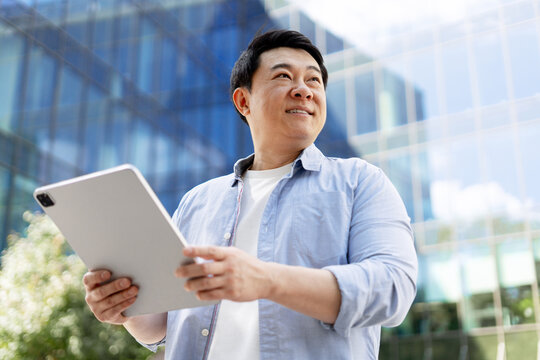 Asian businessman using tablet and looking up in front of office buildings