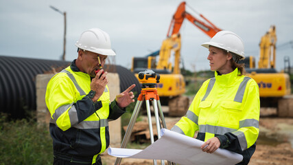 The survey team is using a theodolite and road construction plans. Civil engineers are measuring with surveying tools during the construction