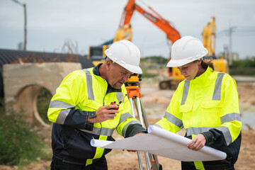 The survey team is using a theodolite and road construction plans. Civil engineers are measuring with surveying tools during the construction