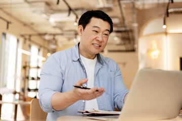 Asian businessman having video call and explaining something using laptop in cafe