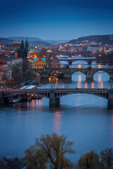 Obraz premium Evening view of illuminated bridges over Vltava River in Prague, Czech Republic, with historic towers, city lights, and reflections creating romantic atmosphere.