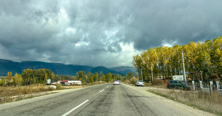 Country Road with Cars and Autumn Trees Under a Heavy, Overcast Sky