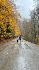 Man and Woman Walking Together on a Wet, Leaf-Strewn Road in the Autumn Woods