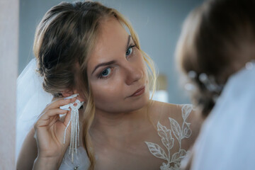 Bride looks into a mirror while adjusting her earring, wearing a lace gown and veil. A quiet, intimate moment of preparation before the ceremony.