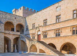 Naklejka premium Inside the historic Palace of the Grand Master of the Knights in Rhodes Old Town, Greece. Ornate stone arches frame a sunlit courtyard with an ancient sphinx statue.