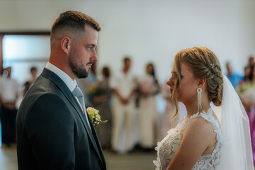 The bride and groom look into each others eyes during their indoor wedding ceremony, surrounded by softly focused guests in the background.