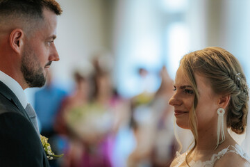 The bride and groom look into each others eyes during their indoor wedding ceremony, surrounded by softly focused guests in the background.