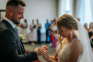A close-up moment of a bride gently placing a gold wedding ring on the groom’s finger during their marriage ceremony. Intimate and symbolic gesture.