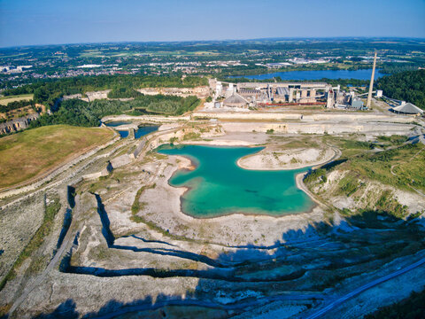 Aerial view of a striking turquoise lake nestled amidst the stark white of a quarry contrasted with the lush green landscape, Valkenburg, Limburg, Netherlands.