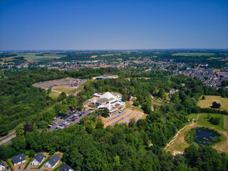 Aerial view of Thermae 2000 gleaming amidst lush greenery under a vast sky, contrasting with the townscape in the distance, Valkenburg, Limburg, Netherlands.