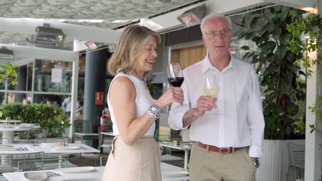 Mature couple sampling wine, sharing conversation while seated at stylish outdoor restaurant, experiencing culinary moment with comfortable intimacy