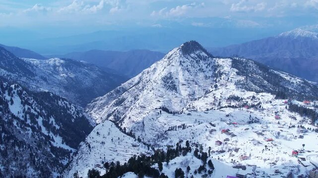 Stunning aerial view of a snow-covered mountain village, with homes dotting the landscape and majestic peaks in the distance. Malam Jabba hill station.