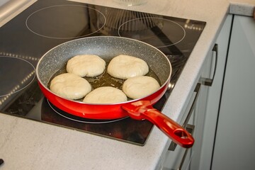 Cooking process featuring dough balls frying in a red skillet on a modern stovetop, showcasing culinary techniques and kitchen environment with focus on food preparation