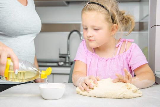 Young girl in pink shirt is engaged in baking, kneading dough on a kitchen countertop while an adult pours oil into a bowl, creating a warm family cooking atmosphere - Powered by Adobe