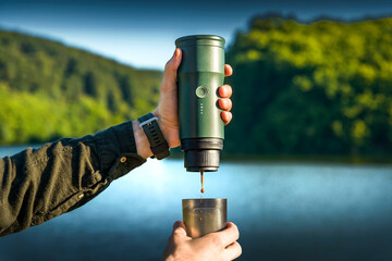 Close-up of hands brewing coffee with a portable espresso maker in a mountain setting