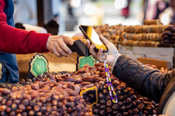 Close-up of a mobile phone payment at a market stall selling dates and dried fruits, blending traditional shopping with modern contactless technology.