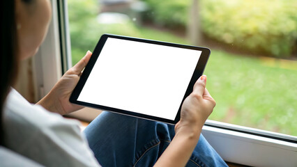 Asian woman holding black tablet with blank white screen near window for mock up