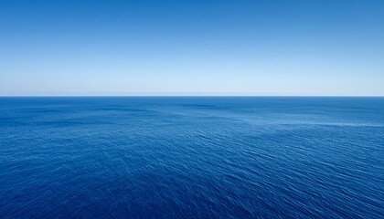 Obraz premium Vast, tranquil ocean scene under a clear, azure sky. The horizon line divides the deep blue water and the bright, cloudless sky.