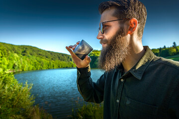 Bearded man drinking morning coffee outdoors with sunglasses, surrounded by mountains
