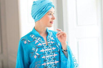 Bride is looking out the window waiting for the groom. Woman in blue colored clothes and turban of the east asian type.