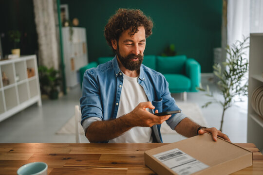 Man scanning package bar code with smart phone at home