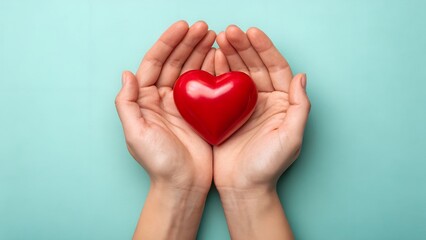 Fototapeta premium Caring hands gently hold a vibrant red heart on a soft blue background.