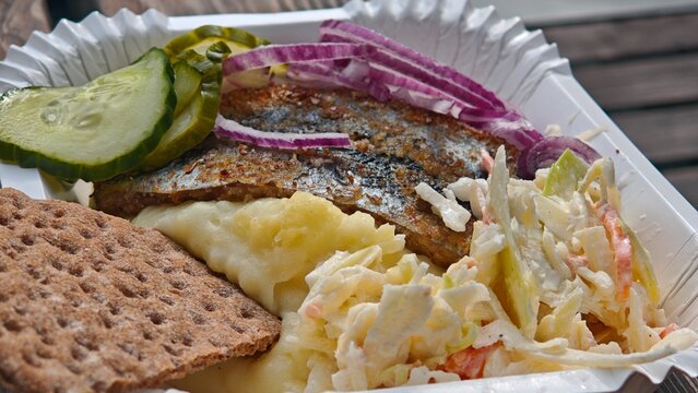 Traditional fried herring served with mashed potatoes, pickles, red onion and coleslaw in a takeaway box. Scandinavian street food concept featuring a rustic and hearty meal with local ingredients