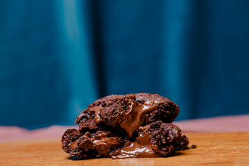 Decadent chocolate cookies with molten chocolate centers, stacked on a wooden board against a blue backdrop. Indulgent dessert. Soft focus for appeal.