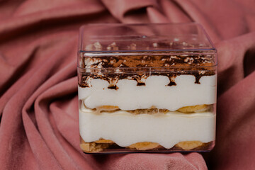 Dessert Delight: A delectable confection in a transparent container, showcasing layers of creamy filling and cocoa dusting on a pink backdrop. Sweet treat.