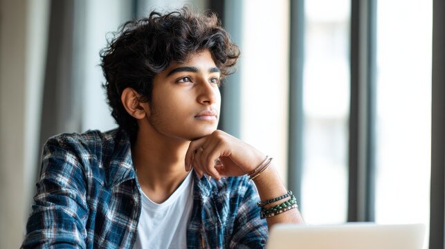 Young indian dreamy thoughtful student looking away working on laptop in office coworking space classroom. Hispanic student using computer for remote learning online training., no logos, no brands