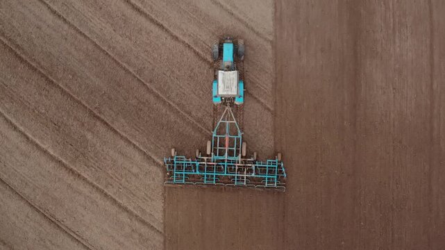 Shot from above of the tractor with a grain seeder is working in the field
