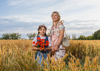 Mother and daughter in traditional Bavarian dresses standing in golden wheat field. Warm and joyful...