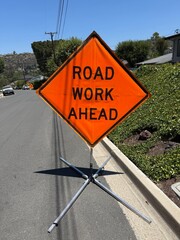 Road Work Ahead Sign: Bright orange road sign warning of upcoming construction zone on public street