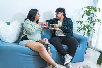 Pregnant woman with prosthetic leg enjoying tea with husband on sofa
