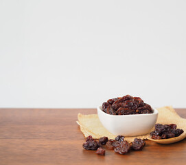 Raisins in white bowl on wooden table background. Dry raisins.