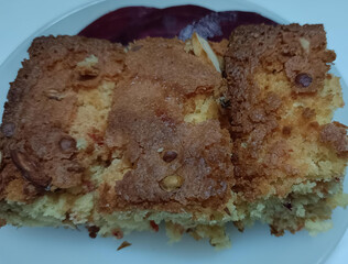 Close-up of soft and moist tea cake slices loaded with dry fruits and nuts, served on a white plate. Golden-brown crust with rich texture.