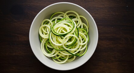 Flat lay of fresh raw zucchini noodles in a white ceramic bowl. Healthy, vegan, keto and gluten free pasta alternative for clean eating on a dark wooden kitchen table background.