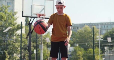 child dribbling basketball outdoor court. Child playing basketball shows skillful control. Young athlete dribbling highlights athletic. Sunny court scene illustrates basketball practice slow motion